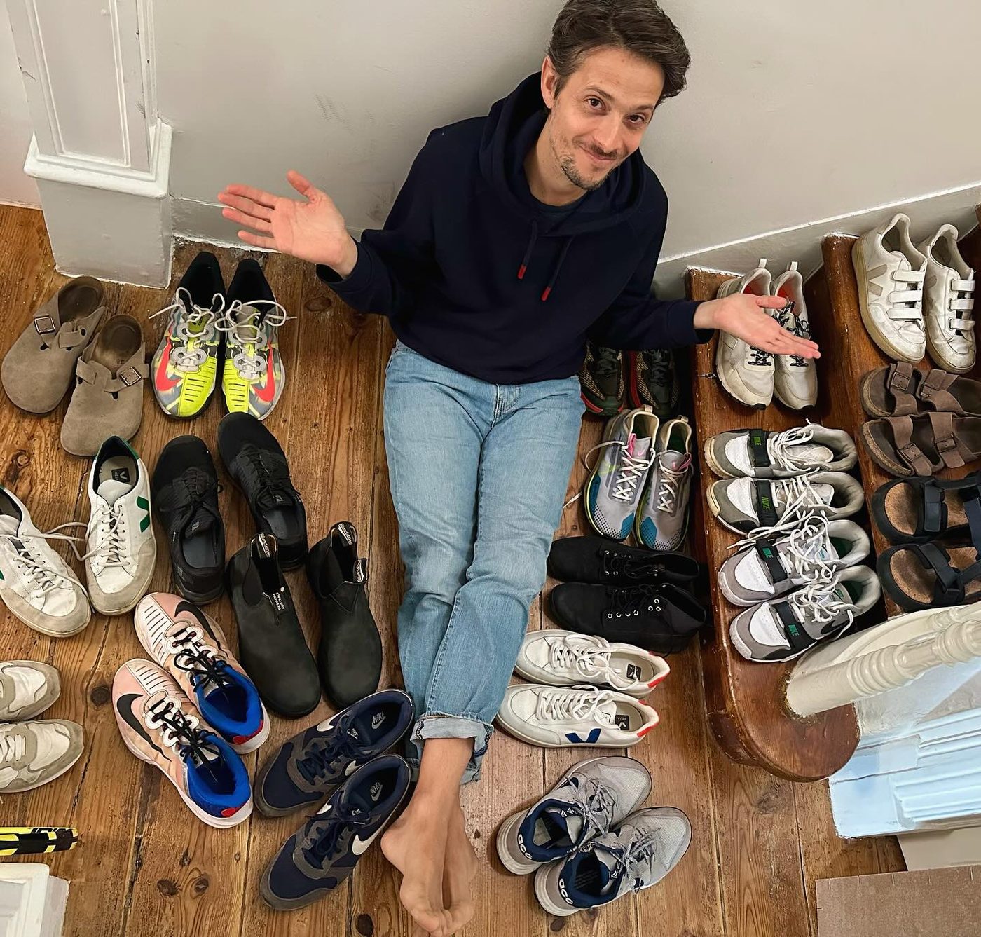 Jonathan assis par terre, haussant les épaules au milieu d'une vingtaine de paires de baskets