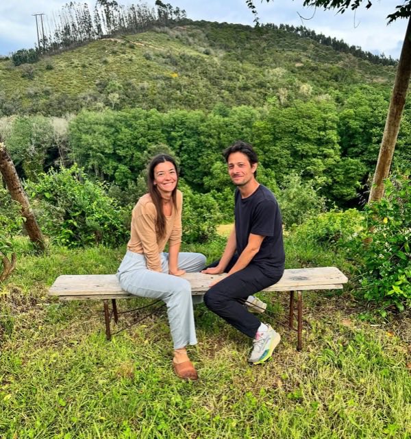 Jeanne et Jonathan assis sur un banc en bois, dans l'herbe, devant une colline
