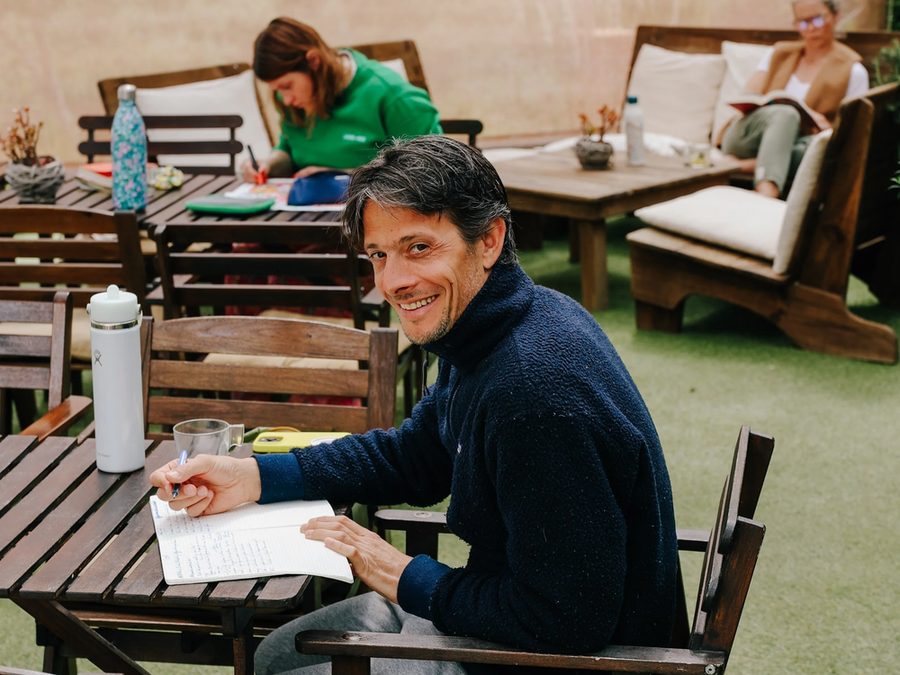 Jonathan, souriant, écrit dans un carnet à une table en terrasse pendant une retraite