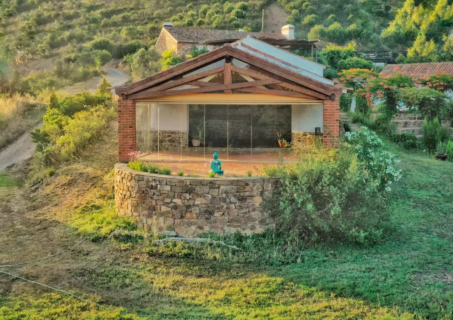 Un pavillon vitré au toit de bois, entouré de verdure, avec une statue turquoise